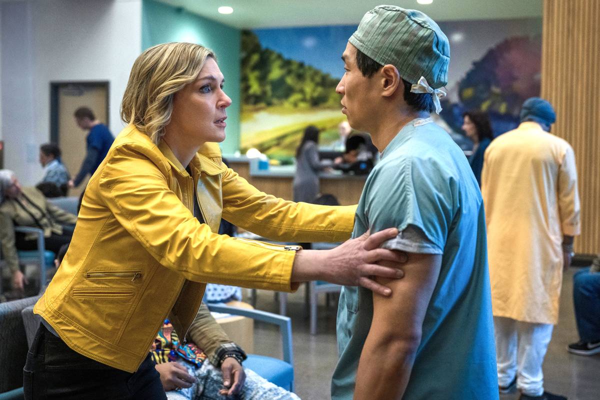 rhea seehorn s carol holding a doctor by their arms looking worried in an er lobby in pluribus 1